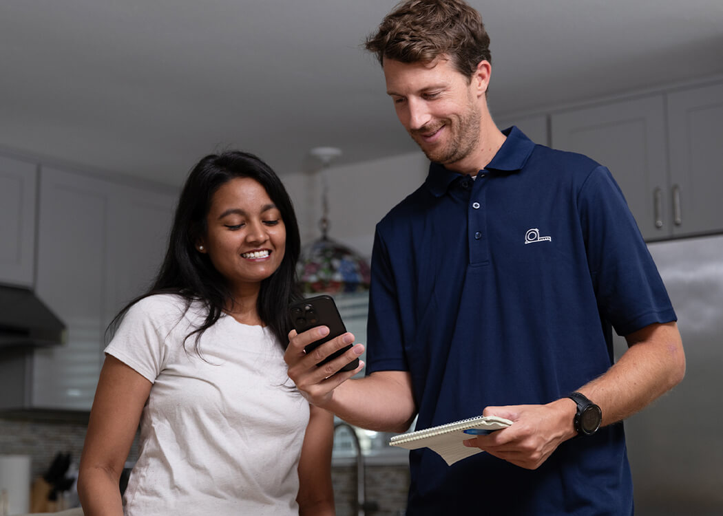 Service person in female customer's kitchen measuring space using Lowes Measure Your Space mobile interface. 