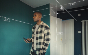 Male in home measuring his room's dimensions with his mobile device. 