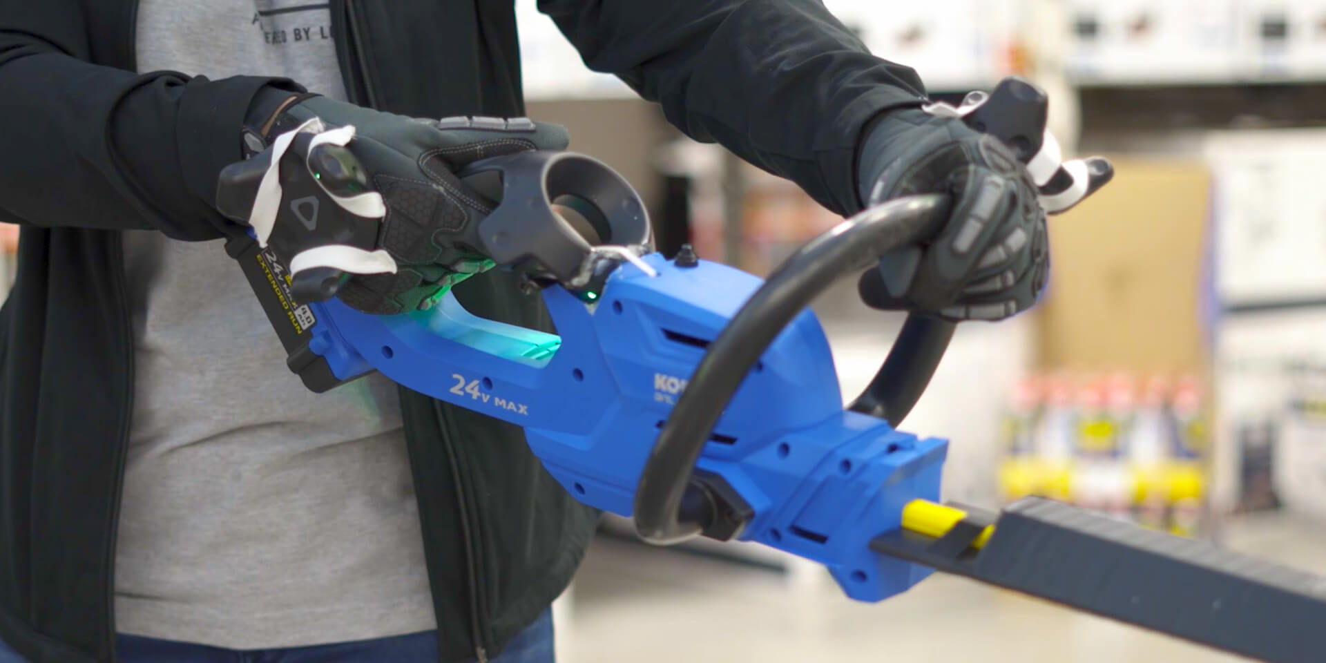 Customer holding a powertool-shaped controller learning how to trim hedges in a VR environment. 