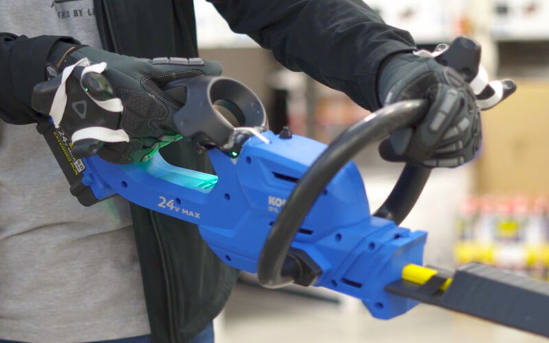 Customer holding a powertool-shaped controller learning how to trim hedges in a VR environment. 